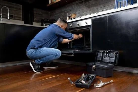 Technician repairing a kitchen oven with tools nearby